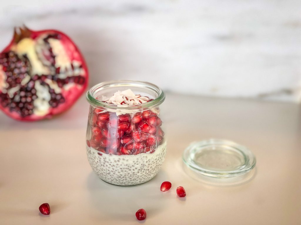 Small Weck jar with chia pudding and pomegranate in front of a cut pomegranate