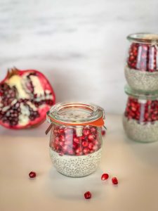 One close up jar of chia pudding with a pomegranate and more jars in the background