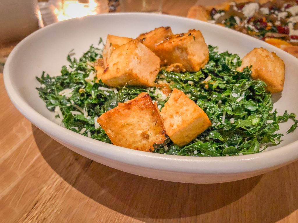 A round white bowl filled with kale and cubes of browned tofu