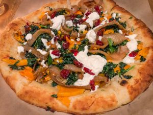 A pizza topped with onions, squash, ricotta and dried cranberries