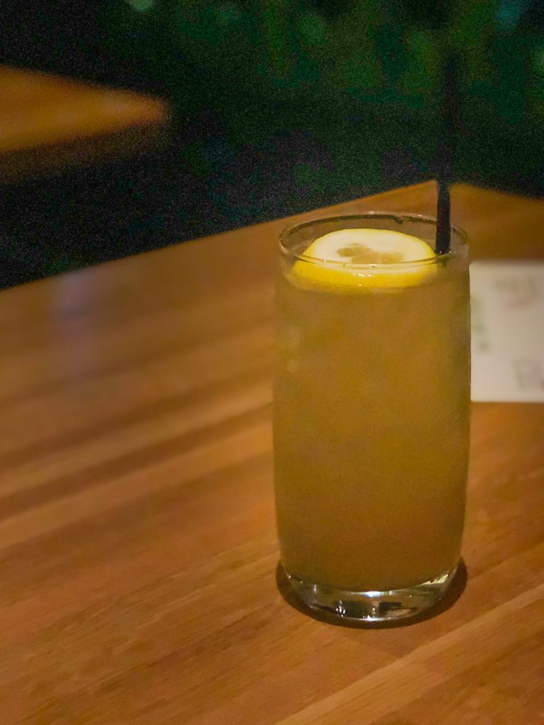A glass of iced tea garnished with lemon and a straw on a wooden table