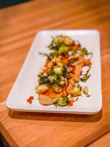 Bread topped with squash, Brussels sprouts and hazelnuts on a white rectangular plate