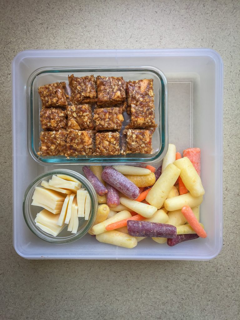 Square plastic container with granola bars, baby carrots, and mozzarella cheese