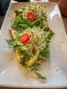 White rectangular plate with toast topped with sprouts, tomato and avocado