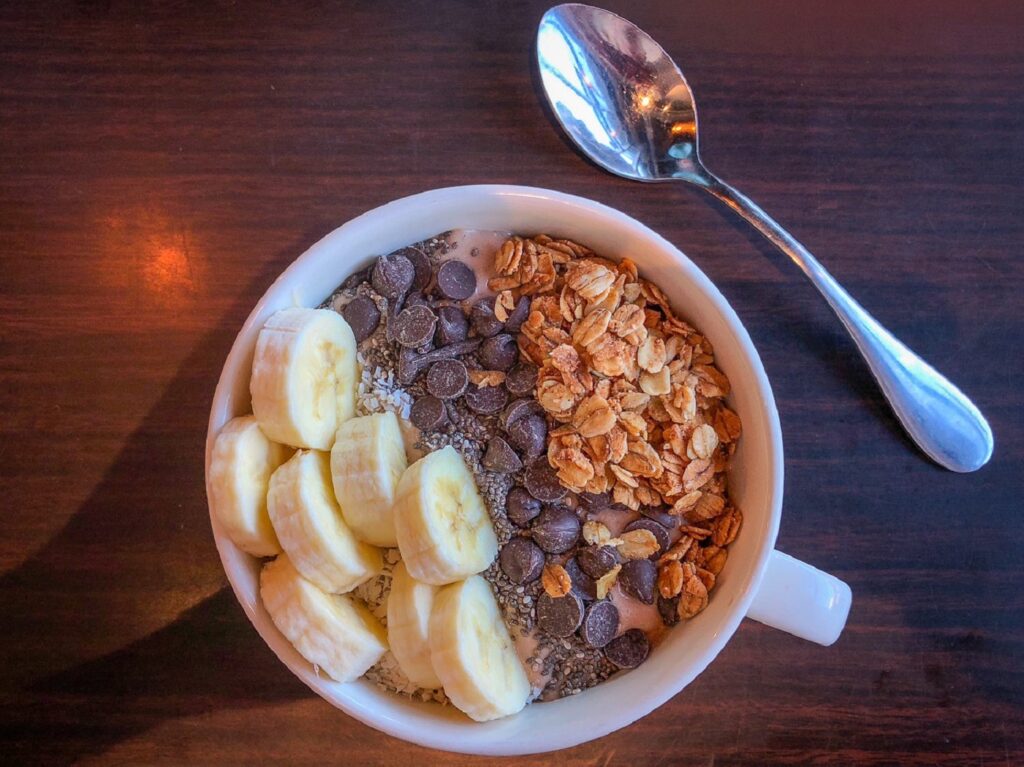 Smoothie bowl and spoon, topped with banana, granola and chocolate chips