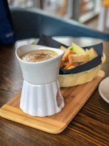 Basket of apple slices and bread next to a small pot of cheese fondue