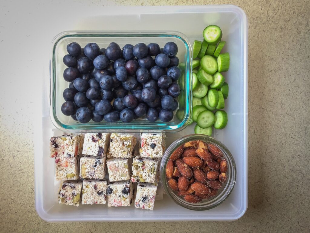 Tupperware filled with blueberries, nuts, and veggies