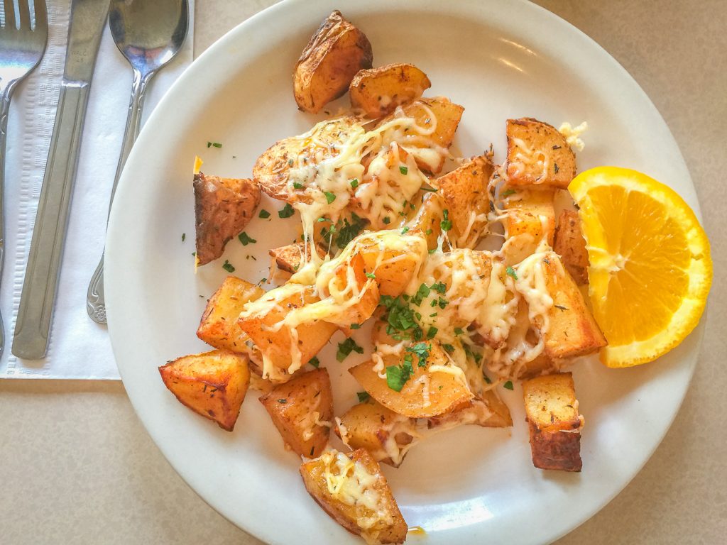 White plate covered with roasted potatoes and melted white cheese