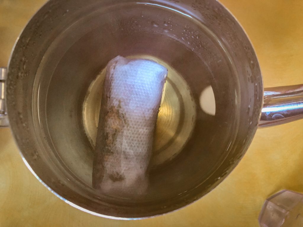 Top down view of a teapot with the lid open filled with water and a teabag