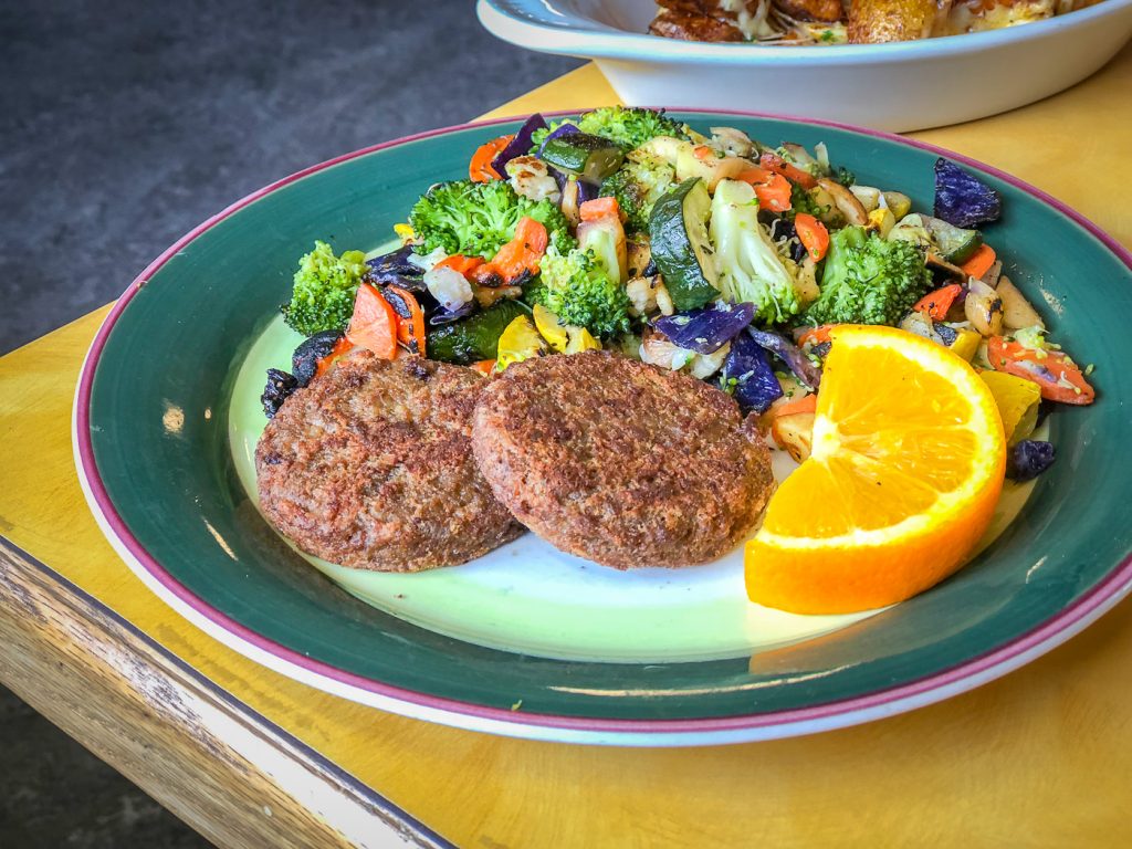 Green rimmed plate with two sausage patties, and a colorful pile of roasted veggies