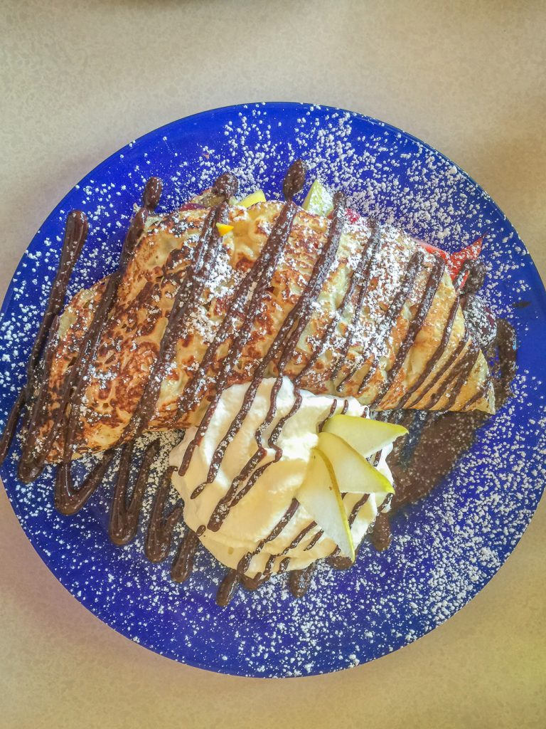 Blue plate with crepe and whipped cream drizzled with chocolate
