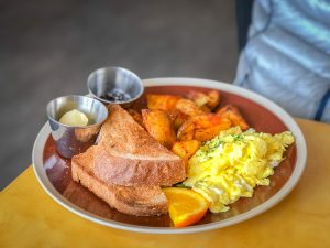 Brown plate with scrambled eggs, whole wheat toast, and roasted potatoes