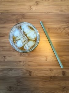 Top down photo of glass filled with iced tea and ice next to a bamboo straw