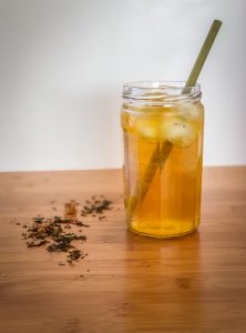Side view of a glass of iced tea with a bamboo straw and loose leaf tea sprinkled next to it