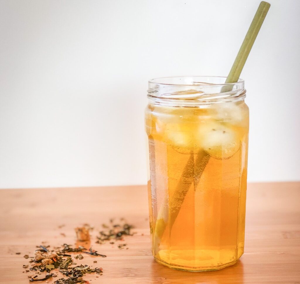 Loose tea on a table next to a glass of iced tea with a straw