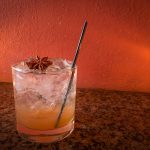 Glass with ice and apple date vinegar with a small straw garnished with a star anise