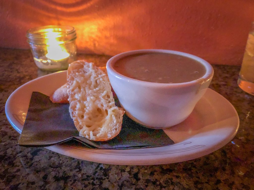 Bowl of soup on a plate with a napkin and two pieces of baguette with melted parmesan
