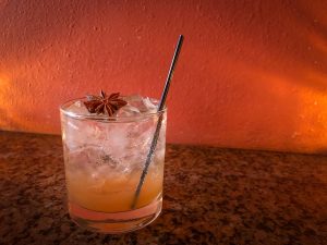 Glass with ice and apple date vinegar with a small straw garnished with a star anise