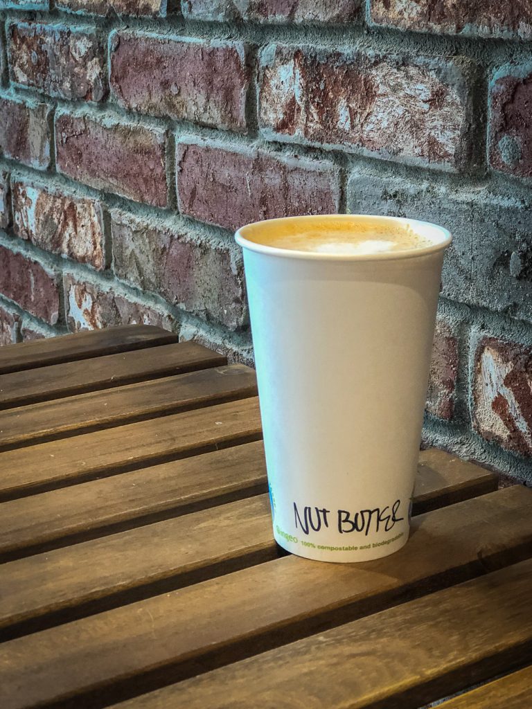 Wooden table with a paper coffee cup on it that says nut butter