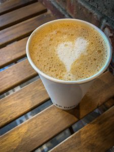 Top down picture of a latte in a paper cup with a heart drawn in the foam