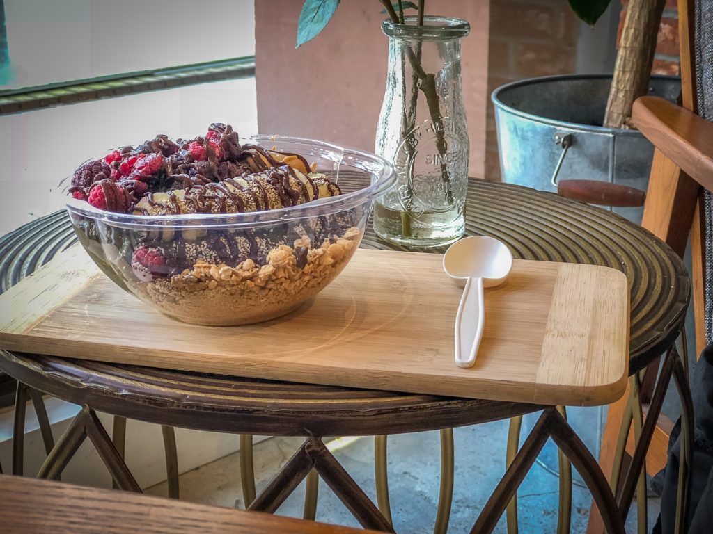 Plastic bowl filled with smoothie and fruit on a wooden tray on a table