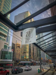 Glass covered walkway with a sign hanging down for Melu Juice