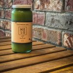 Bottle of green juice on a wooden table in front of a brick wall