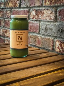 Bottle of green juice on a wooden table in front of a brick wall