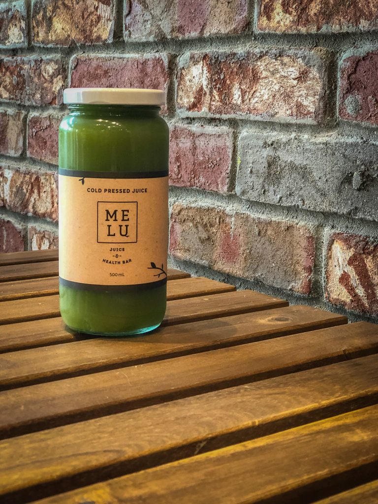 Bottle of green juice on a wooden table in front of a brick wall