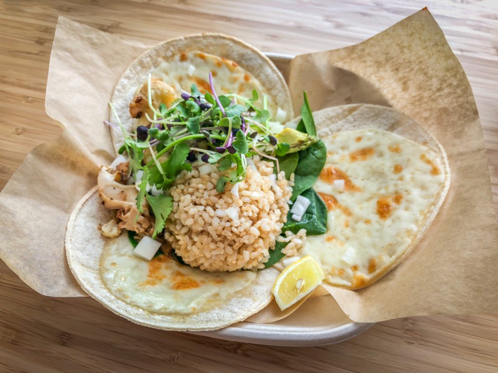 3 tortillas covered in melted cheese in a bowl topped with brown rice and cauliflower