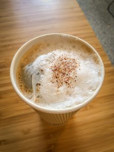 Paper cup filled with tea and topped with foam on a bamboo table