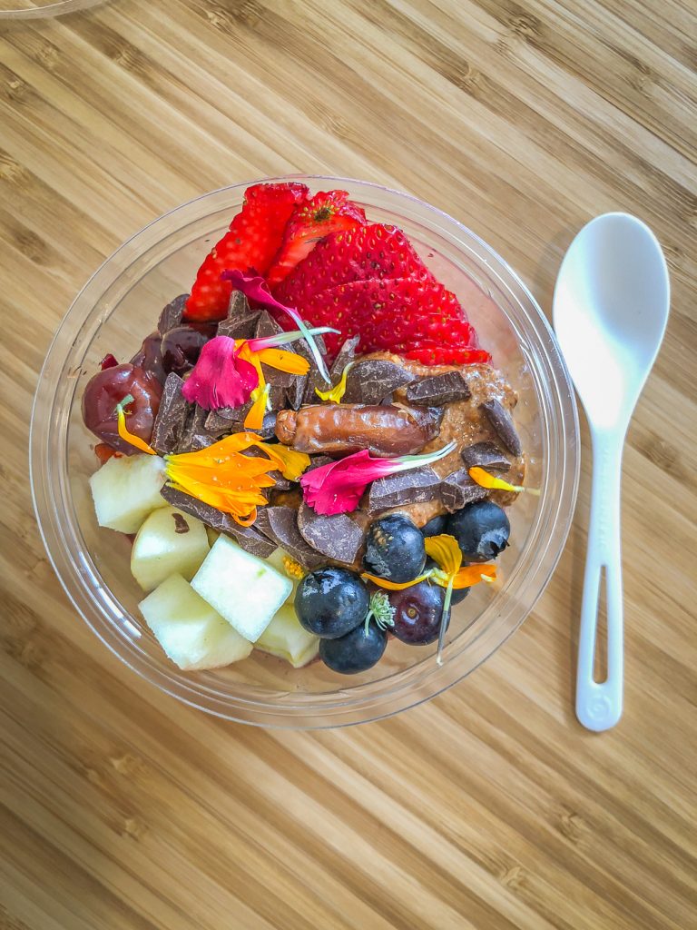 Plastic bowl filled with apples, blueberries, strawberries, dark chocolate and edible flowers
