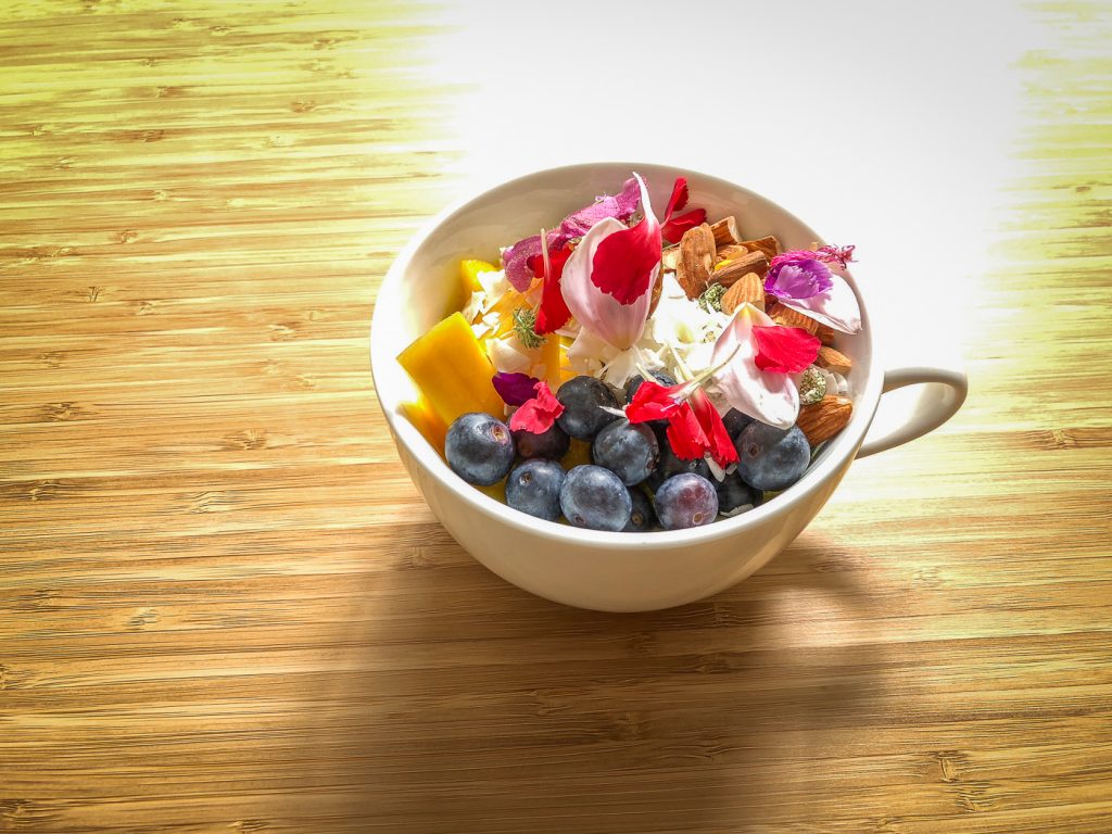 Tea cup filled with fruit, nuts and edible flowers on a table in a ray of sunlight