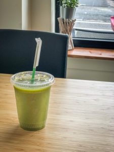 Plastic cup on a bamboo table full of green juice