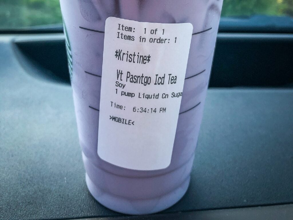 To go cup from Starbucks filled with purple liquid on dashboard of car