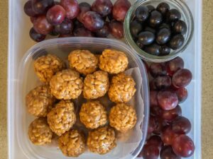 Square tupperware filled with grapes, olives and rice krispie balls