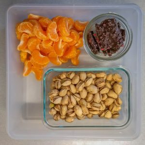 Plastic container filled with orange segments, pistachios and chocolate bark