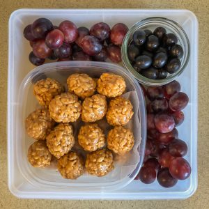 Plastic container filled with rice crispy balls, fruit and olives