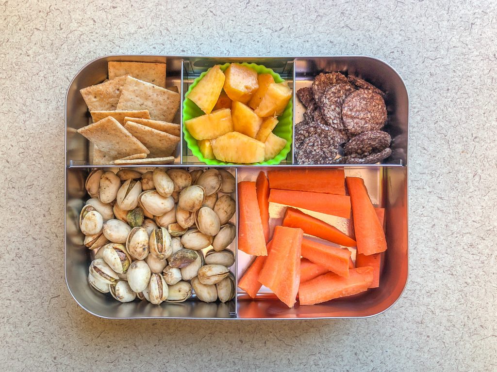 Metal lunch box filled with crackers and pistachios