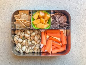 Metal lunch box filled with crackers and pistachios