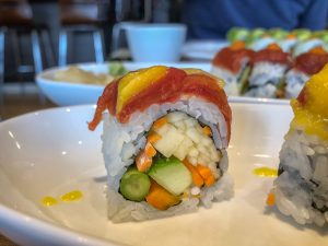 Close up picture of a sushi roll topped with tomato