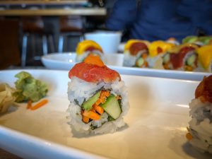 A single sushi roll topped with tomato