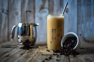 Glass of iced coffee with spilled coffee beans and a French press