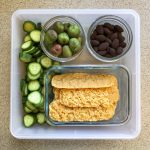 Tupperware filled with kiwi berries, chocolate almonds, parmesan crisps and cucumbers