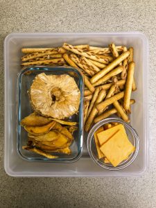 Tupperware filled with pretzels, cheese, dried pineapple and dried mango