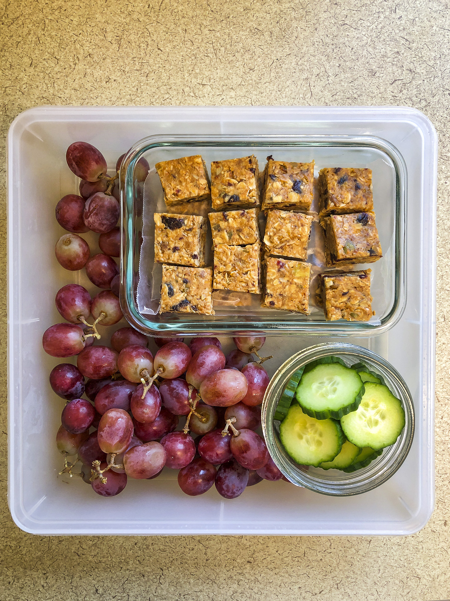 Tupperware filled with granola bars, cucumbers and grapes