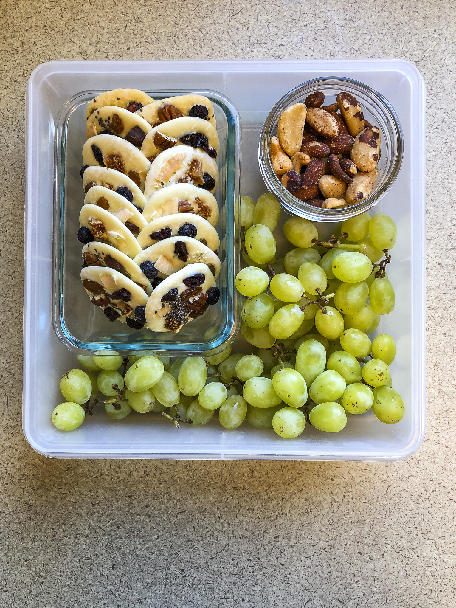 Tupperware filled with white chocolate, nuts and green grapes