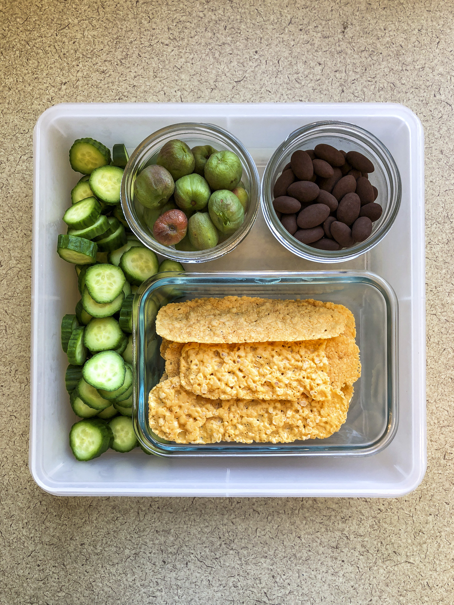 Tupperware filled with kiwi berries, chocolate almonds, parmesan crisps and cucumbers