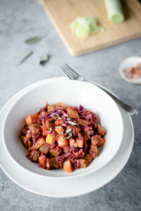 Bowl of veggies and vegan sausage next to a cutting board