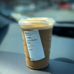 Portrait shot of a cup of iced coffee in focus on a dashboard with a blurred background
